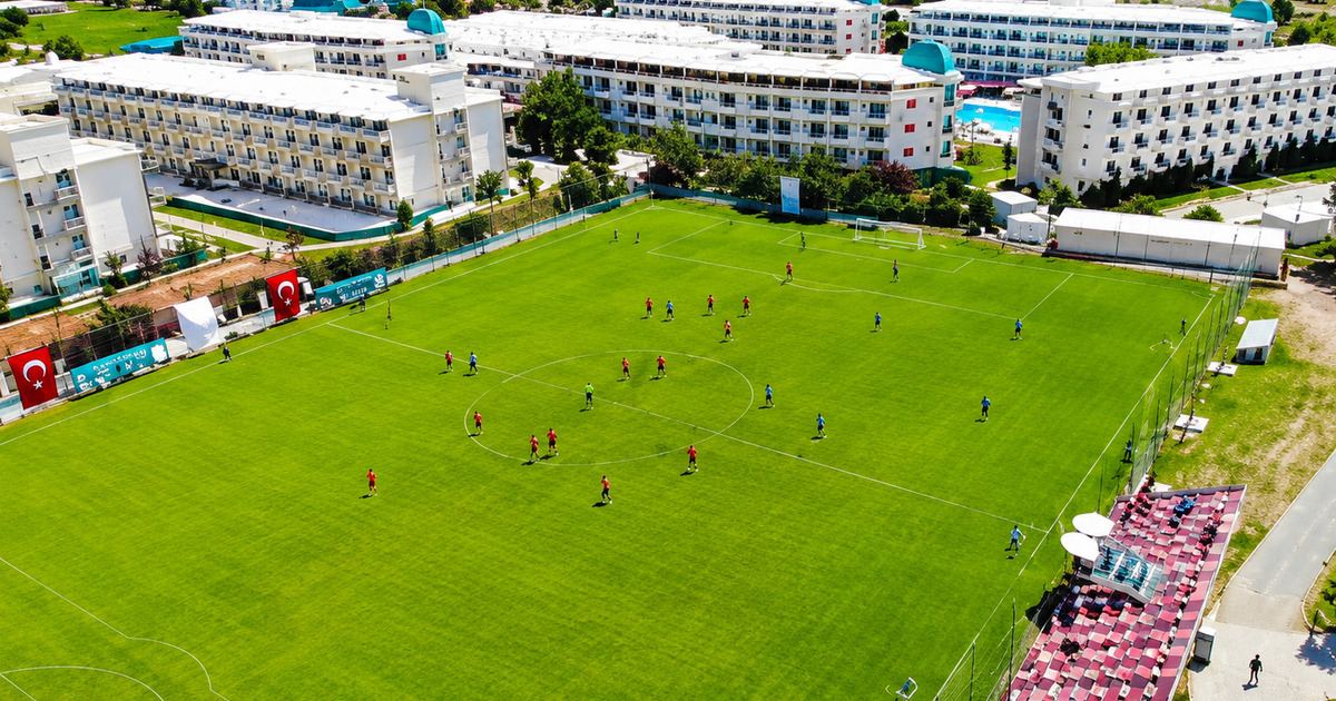 Aerial view of football match in progress at the Kemer sports complex with hotel buildings visible